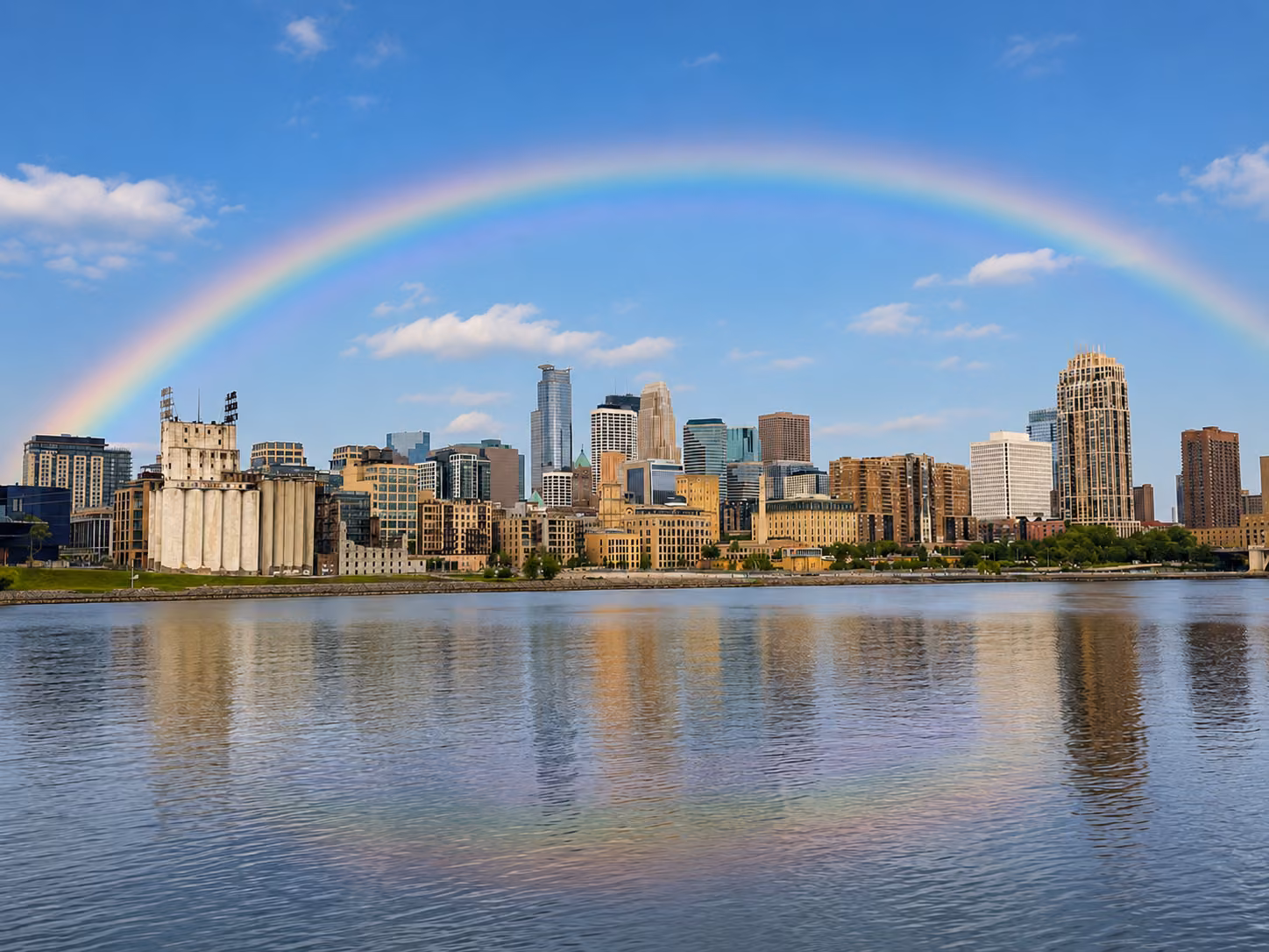 A rainbow arches over the Minneapolis skyline and its reflection in the Mississippi River.